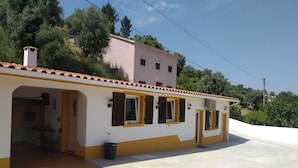 Edifici de dos pisos amb façana beig i groga, pati enrajolat i una petita zona d'seients a l'aire lliure.