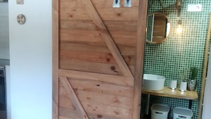 Una porta corredissa de fusta que dona a un bany amb una paret de rajoles verdes, un mirall i una estant amb productes de tocador.