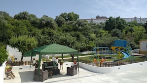 Un parc amb una àrea de jocs, zona de seients i un edifici al fons.