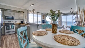 Ett modernt kök med vitvaror i rostfritt stål, en matplats med vävda bordstabletter och utsikt över havet.
