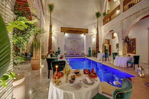 Ein Poolbereich im Innenbereich mit Essbereich, umgeben von dekorativen Pflanzen und traditionellen marokkanischen Fliesen.