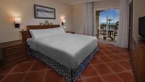 Habitación de hotel con una cama grande, dos mesitas de noche, un televisor y un balcón con vistas a palmeras.