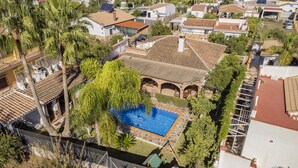 A residential area with a swimming pool surrounded by lush greenery and a tiled-roofed house.