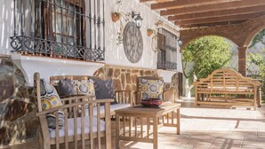 An outdoor patio with stone walls, wooden furniture, and a tiled floor.