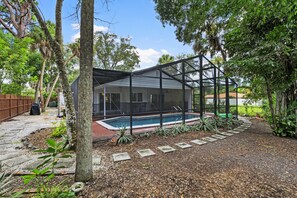 A house with a swimming pool, surrounded by a garden with various plants and a stone pathway.