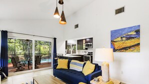 Un salon moderne avec un canapé, une table basse et une vue sur la cuisine et l’espace extérieur.