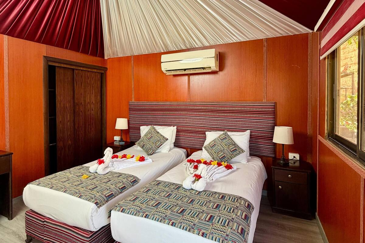 Ein Zimmer mit zwei Betten, einem Deckenventilator, einem Fenster und einer Holztür.