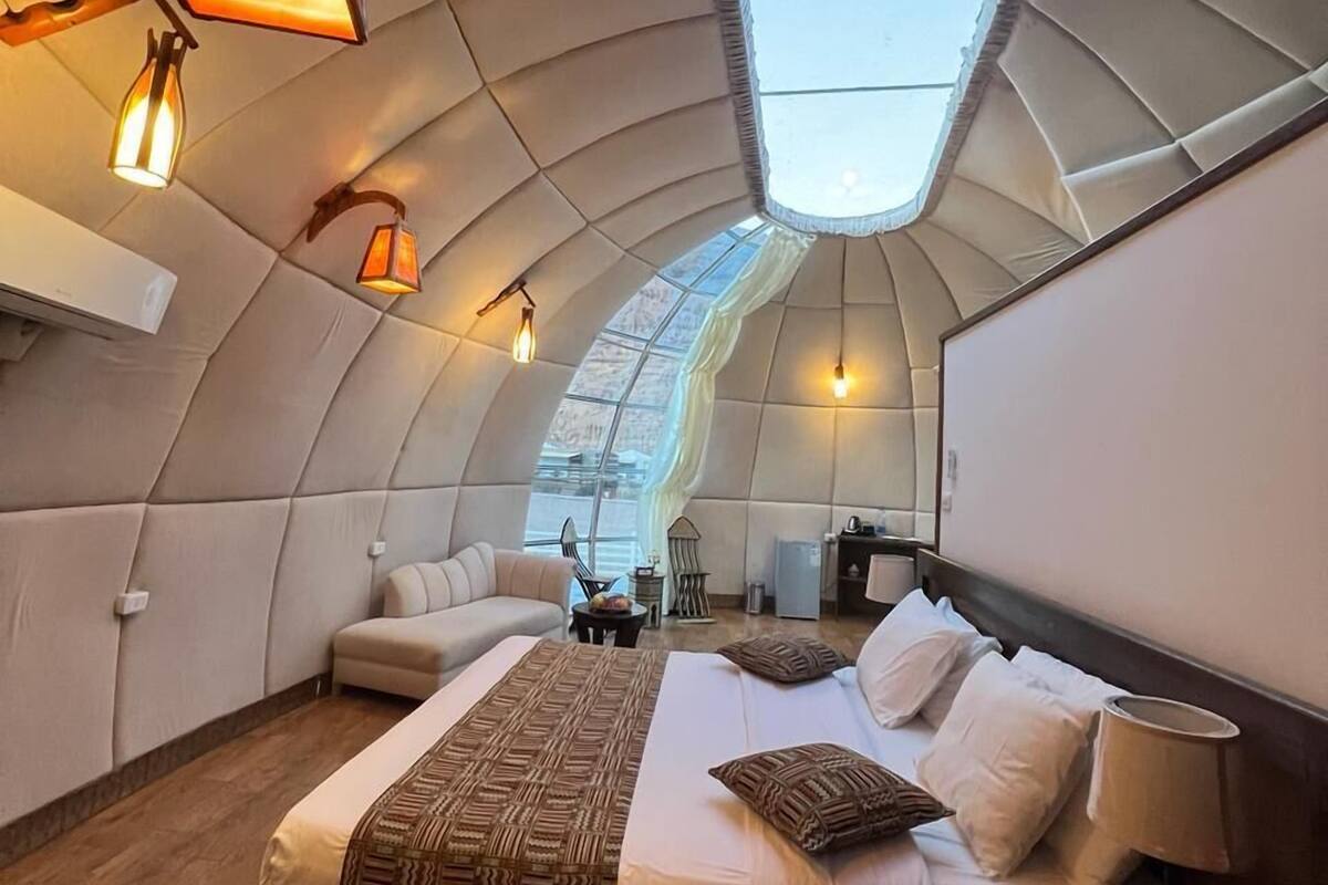 Ein modernes Schlafzimmer mit gewölbter Decke, einem Oberlicht, einem großen Bett mit gemusterten Textilien und stimmungsvoller Beleuchtung.