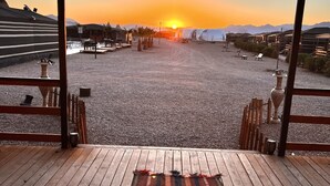 Een zonsondergang uitzicht vanaf een overdekt terras met een houten dek en een gestreept vloerkleed.