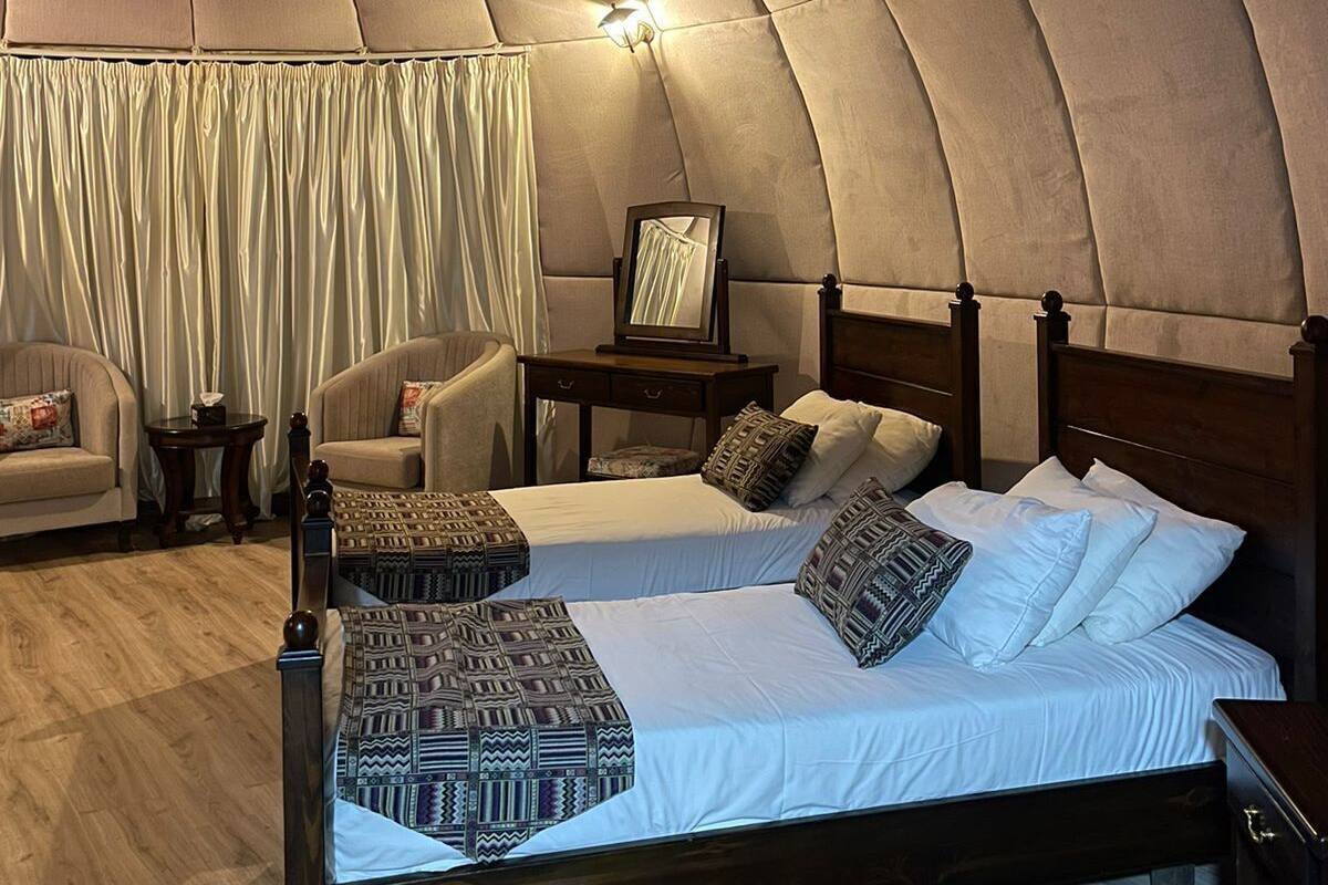Ein gemütlicher, halbkreisförmiger Raum mit einem hölzernen Bett, zwei Stühlen, einem kleinen Tisch und einem Spiegel.