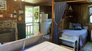Ein gemütliches Blockhauszimmer mit einem Bett, einer kleinen Küchenzeile, einem Korbstuhl und einer Steinwand.