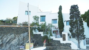 A boat docked near a white building with stone walls and a flag.