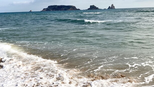 A beach with waves crashing onto the shore and distant rocky outcrops.