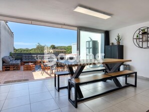 A modern living room with a large sliding glass door leading to a terrace. Inside, there is a wooden dining table with benches, a sofa set, and a cabinet with decorative items. - RENOVATED APARTMENT WITH A LARGE TERRACE FOR 4 PEOPLE (Platja d'Aro)