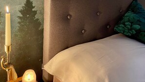 Une chambre à coucher avec un grand lit, une table de chevet avec des bougies et une fresque murale sur le thème de la forêt.