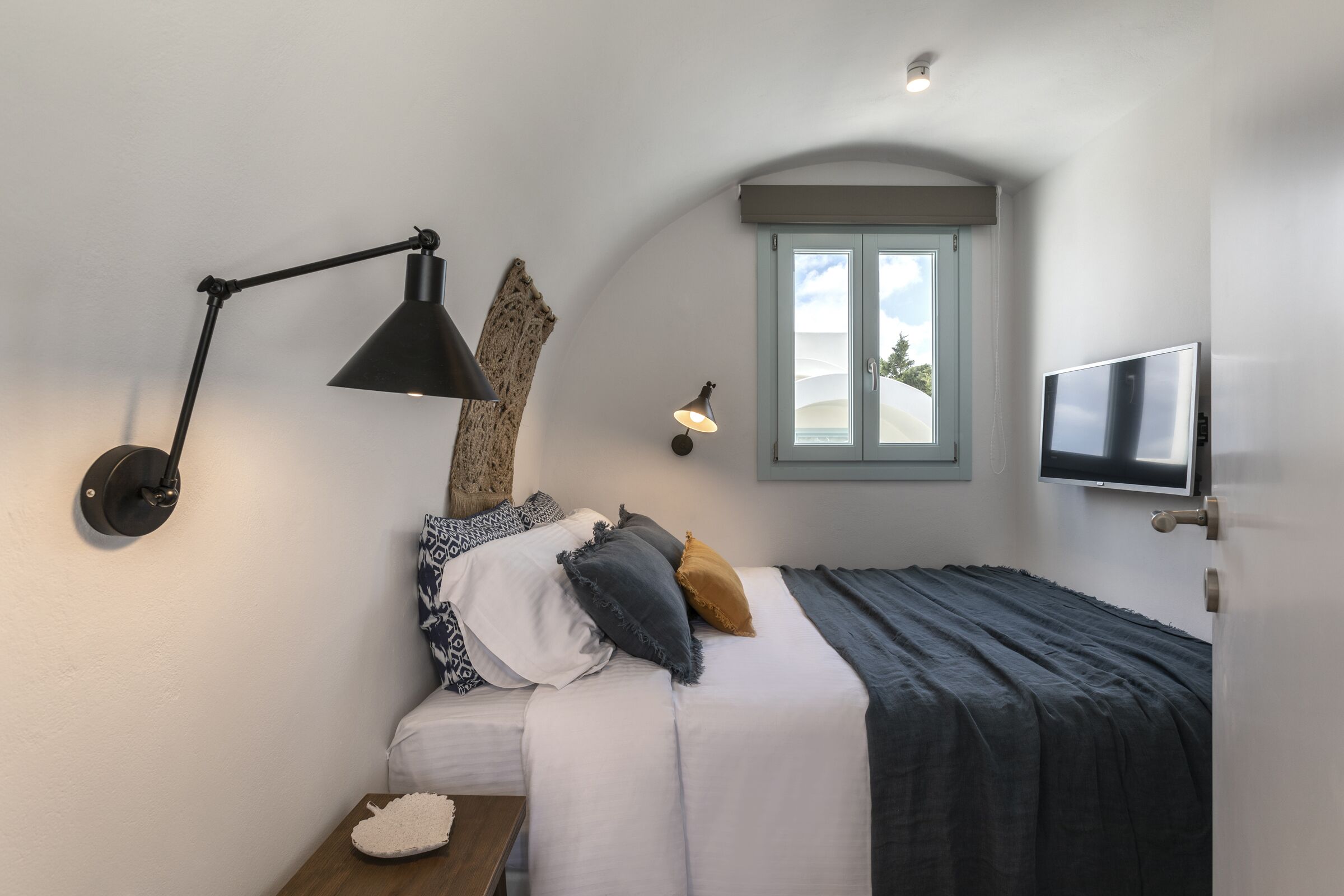 Ein Schlafzimmer mit Bett, Schreibtisch, Lampe, Fernseher und einem Fenster mit Aussicht.
