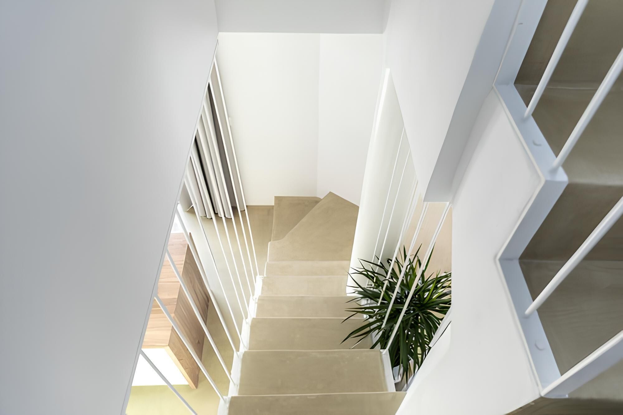 A modern staircase with a geometric design, white railings, and a potted plant at the bottom.