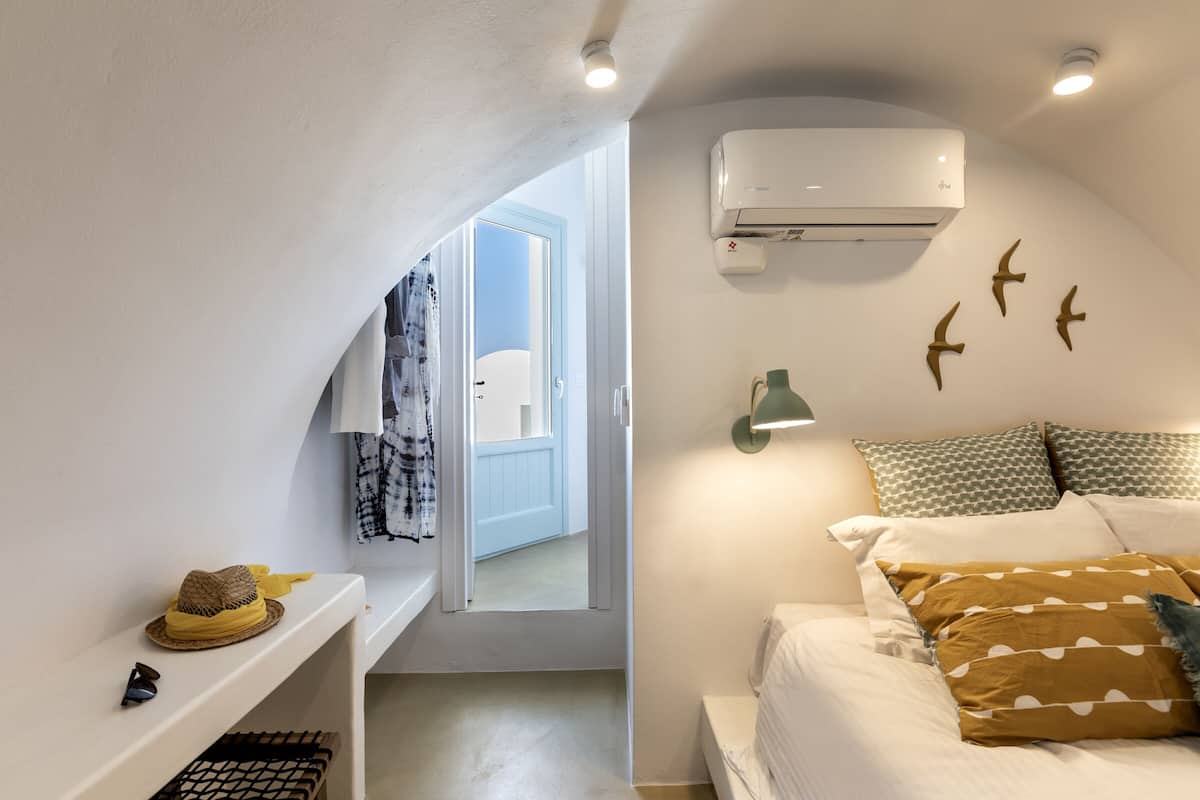 Um quarto com uma cama, ar condicionado, luminária na parede e uma porta que dá para outro cômodo.