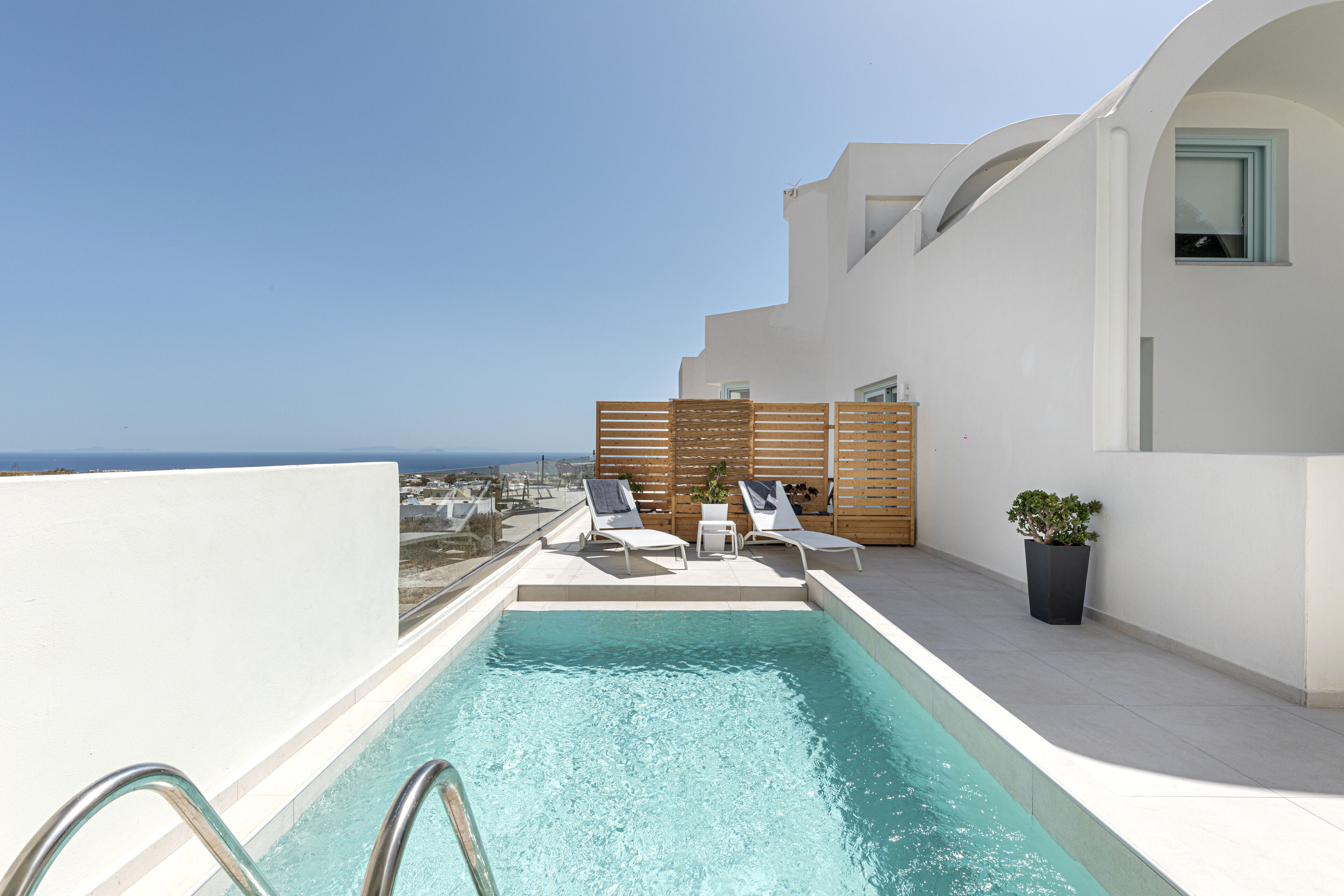 Piscina en la azotea con dos tumbonas y una planta en maceta, con vistas a un paisaje urbano.