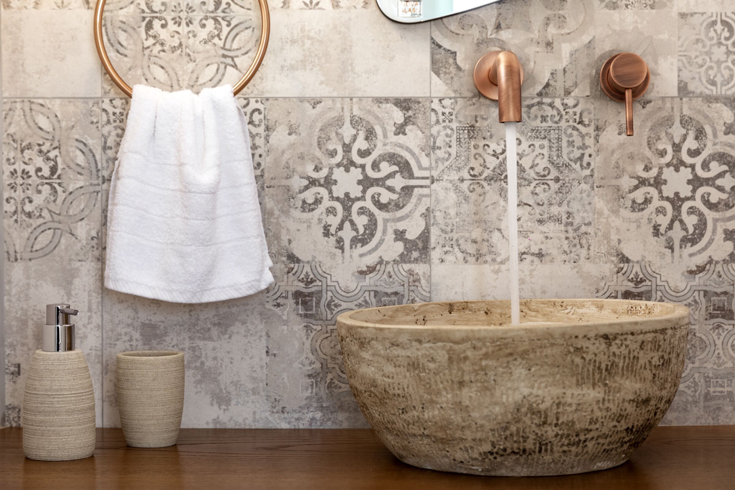 A bathroom with a large stone basin, a towel hanging on a wooden ring, and a soap dispenser.