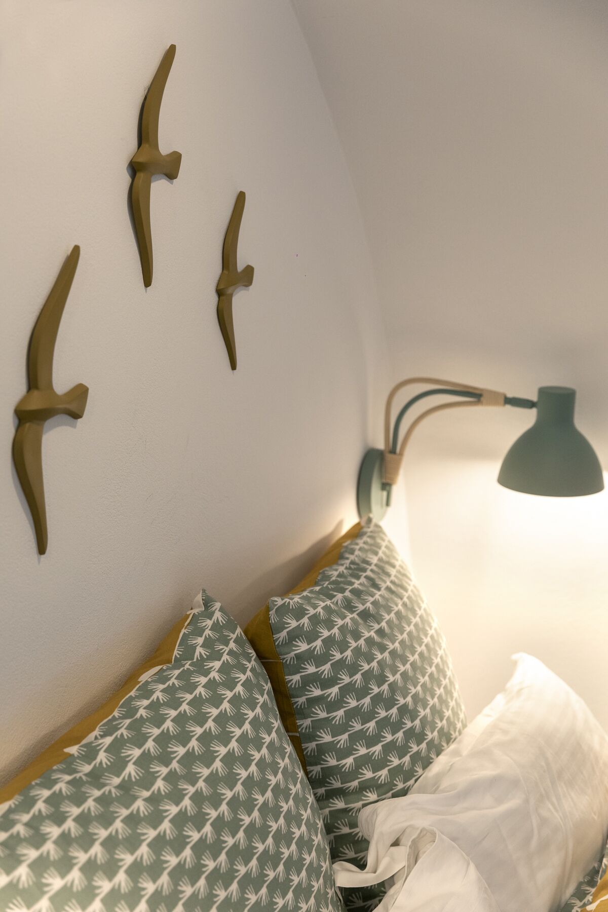 A bed with patterned pillows and a wall-mounted lamp.