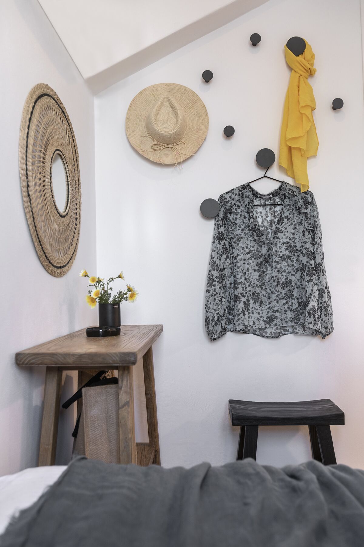 Une chambre à coucher avec un lit, une table en bois ornée d’un vase de fleurs, un chapeau suspendu et un porte-chapeaux fixé au mur.