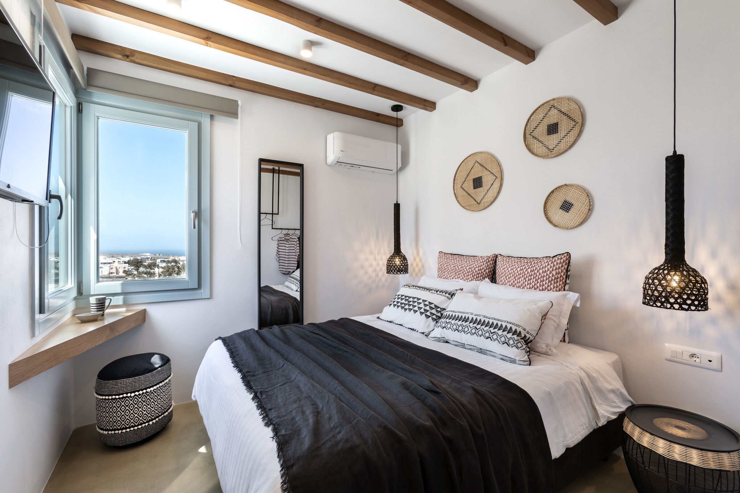 A modern bedroom with a large bed, a window with a view, a hanging light fixture, and a wall-mounted air conditioner.