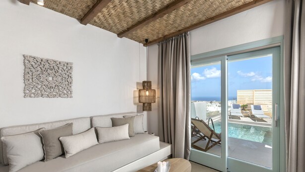 Une chambre moderne avec un canapé, une table basse en bois, un élément décoratif mural et une vue sur une piscine et des chaises de plage.