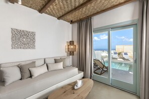 A modern room with a sofa, a wooden coffee table, a decorative wall piece, and a view of a pool and beach chairs. - Santo Bloom Luxury Villas (Santorini)