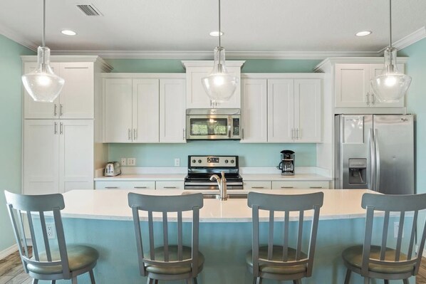 A kitchen with white cabinets, a central island with bar stools, a microwave, stove, and refrigerator.