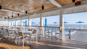 Un espace de restauration en plein air, avec des tables et des chaises, offrant une vue sur une piscine et l’océan.