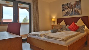 A hotel room with a large bed, a wooden desk, a window with curtains, and a painting on the wall. - Ferienwohnung in Traumhafter Bergkulisse - Appartements Wacker (Bichlbach)