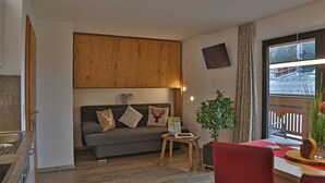 A modern living room with a grey sofa, wooden ceiling panel, a small table with a plant, and a dining area with a red chair. - Ferienwohnung in Traumhafter Bergkulisse - Appartements Wacker (Bichlbach)