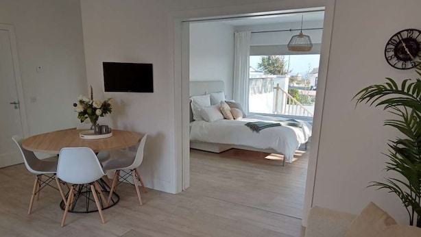 A modern living room with a sofa, a dining area with a round table and chairs, and a bedroom with a bed and a balcony view. - Private coastal space, adjoining family home- with sea views (Galway)