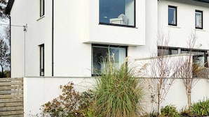 A modern two-story house with a flat roof, large windows, and a gravel driveway. - Private coastal space, adjoining family home- with sea views (Galway)