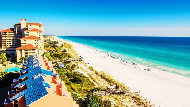 Ein Strandhotel mit mehreren Balkonen, einem Pool und einem Sandstrand.