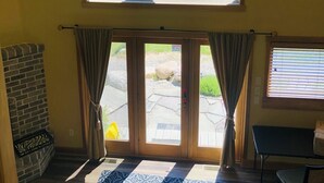 A room with a large arched window overlooking a vineyard, a brick fireplace, and a stone floor with a patterned rug. - Live the Vineyard Life at The Grand View 2 @ Willow Winery (Suttons Bay)