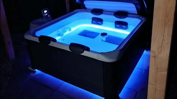 Ein Whirlpool unter einer hölzernen Pergola, umgeben von einer dunklen Außenanlage.