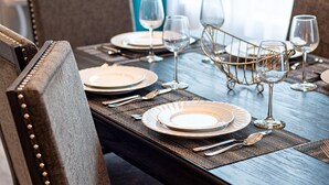 Una mesa de comedor dispuesta con platos, cubiertos y copas de vino, con una cesta metálica decorativa en el centro.