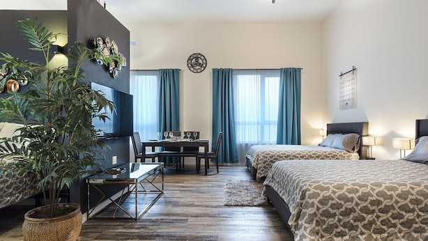 Una habitación de hotel moderna con dos camas, una zona de comedor y una planta grande en maceta.