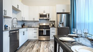 Una cocina moderna con armarios blancos, electrodomésticos de acero inoxidable y un comedor con mesa dispuesta para dos.