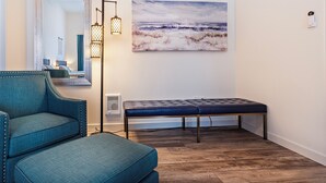 Una sala moderna con un sofá azul, un banco, una lámpara de pie y un cuadro de una playa.