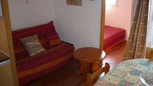 A compact room with a sofa, a small round table, and a bed. - Location Appartement 6 Personnes - Les Angles (Les Angles)
