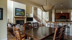 A spacious living room with a wooden dining table and chairs, a fireplace, and a large painting on the wall. - Great Ketchum Condo next to bike path & greenbelt (Ketchum)