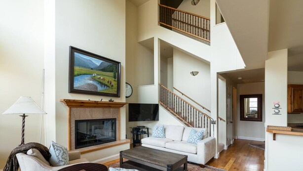 A spacious living room with a fireplace, a sofa, a coffee table, and a TV. There is a staircase leading to an upper level. - Great Ketchum Condo next to bike path & greenbelt (Ketchum)