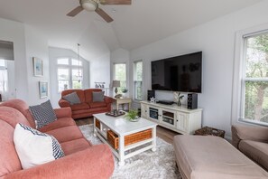 A spacious living room with a large TV, comfortable seating, and a ceiling fan.