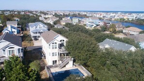 A residential area with houses, a swimming pool, and a body of water in the background. - 1767 - Fox Snooze - Corolla Retreat | Pool, Hot Tub & Beach Walk (Corolla)