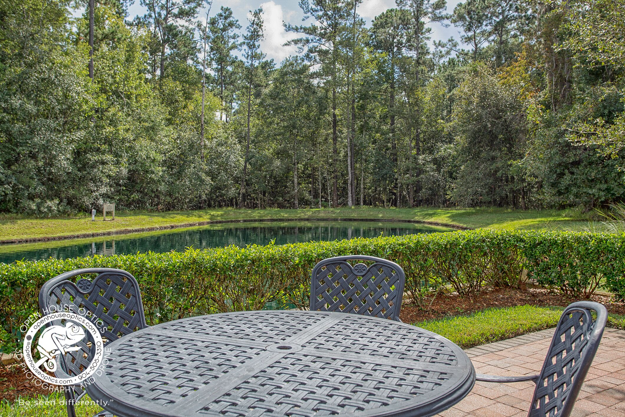 An outdoor seating area with a round table and chairs, surrounded by a manicured lawn and a pond.