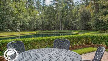 An outdoor seating area with a round table and chairs, surrounded by a manicured lawn and a pond.