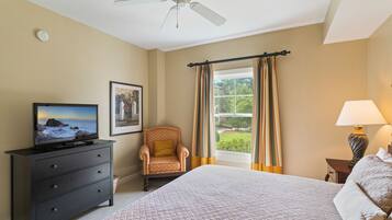 A hotel room with a bed, a television on a dresser, a chair, a window with curtains, and a ceiling fan.
